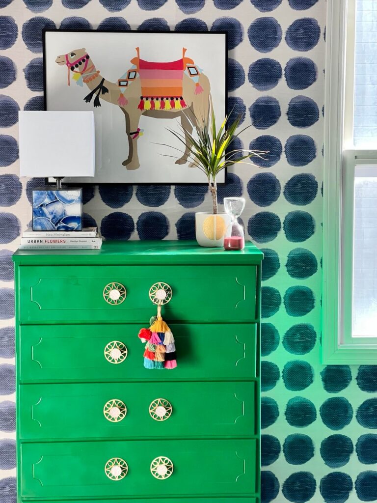 An emerald green dresser against wallpaper with blue dots.
