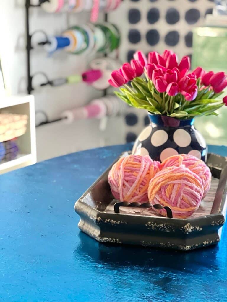 A tray with pink tulips and pink yarn balls on top of the blue foil leaf table.