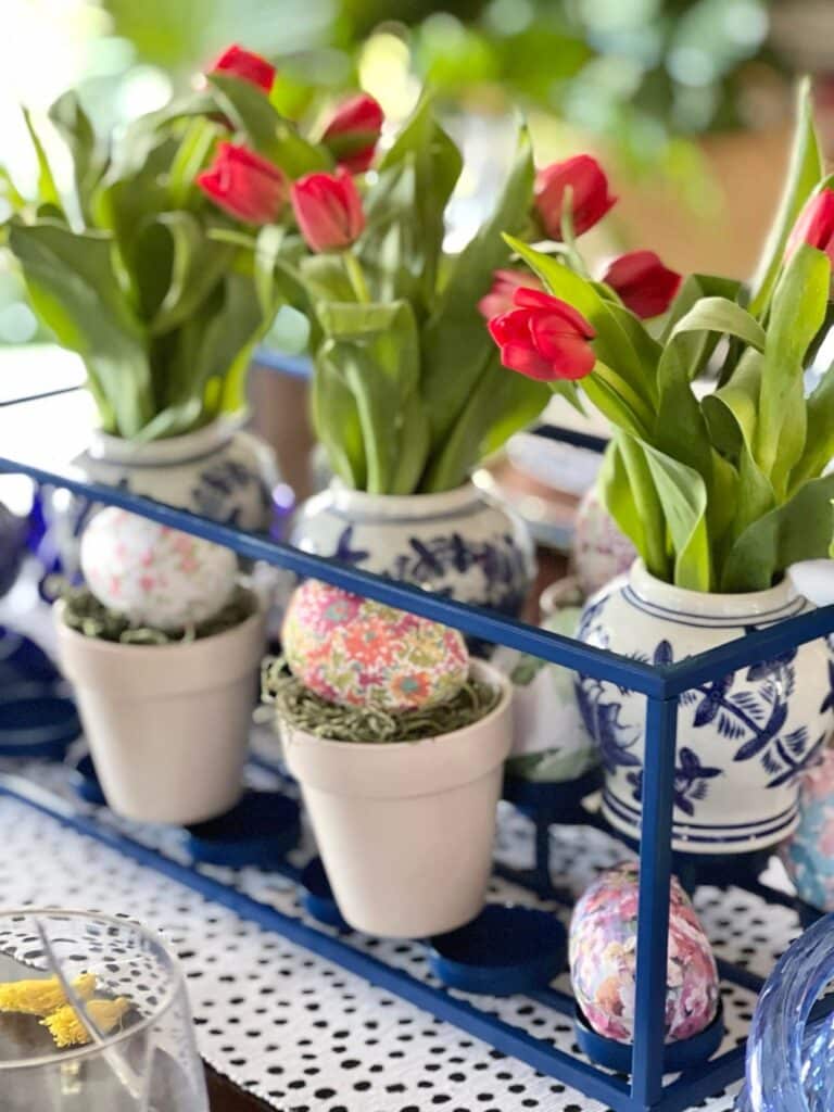 A blue metal candleholder with blue and white pots holding pink tulips for an Easter tablescape.