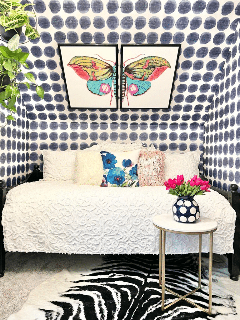 The craft room nook with dotted wallpaper, a black daybed with white coverlet, and a butterfly print hanging on the wall.