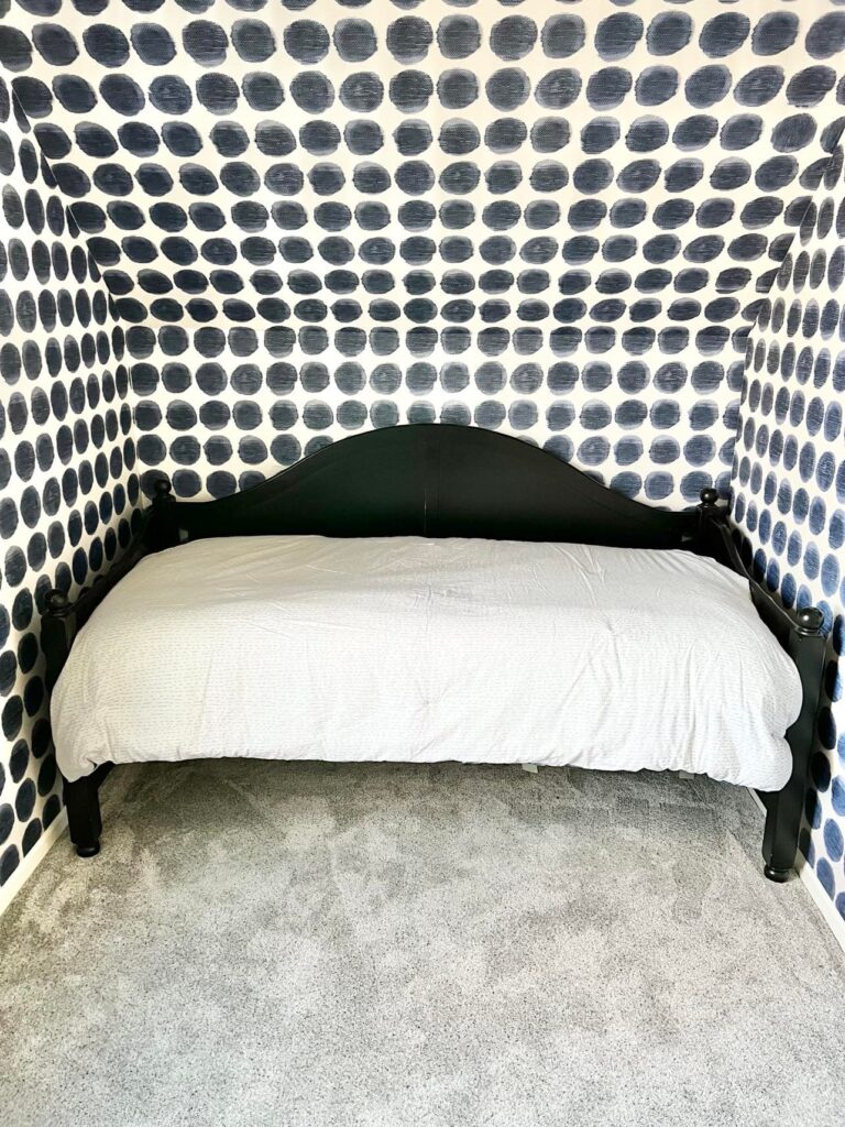 A daybed sitting in a nook with blue and white wallpaper.