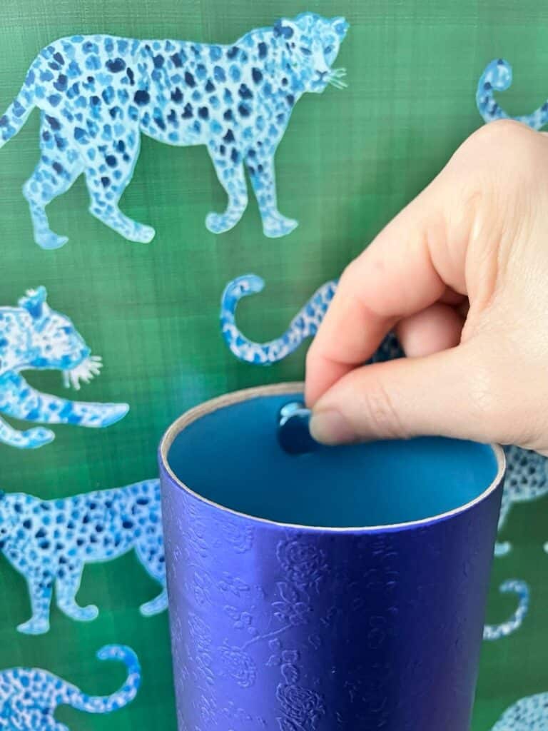Using a push pin to attach a blue cardboard pencil holder.