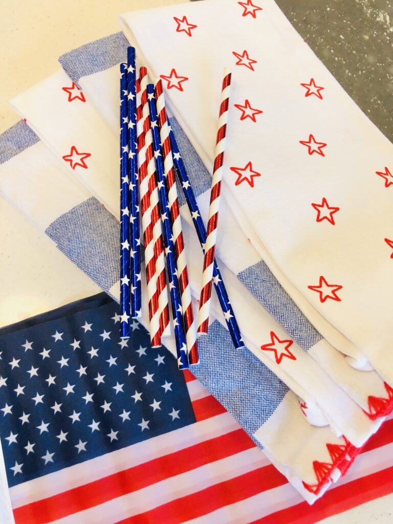 Red and white stripe straws and blue starred straws sitting on top of patriotic themed dish towels as festive 4th of July table decoration ideas.