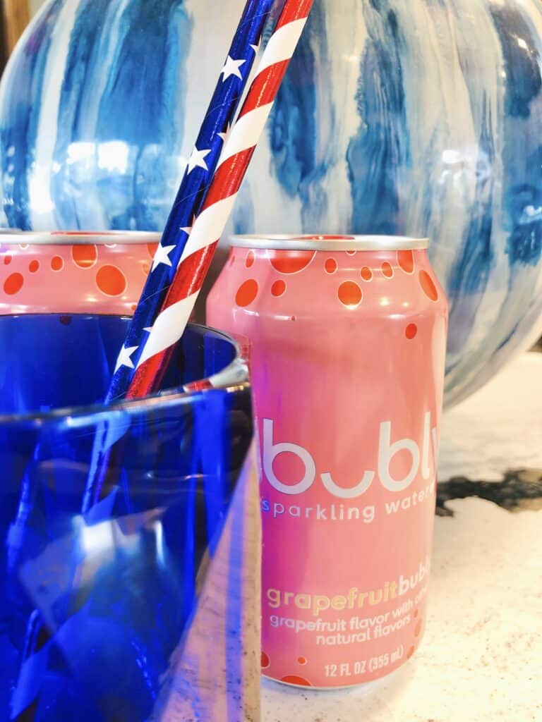 A pink can of sparkling water sitting beside a cobalt blue glass.