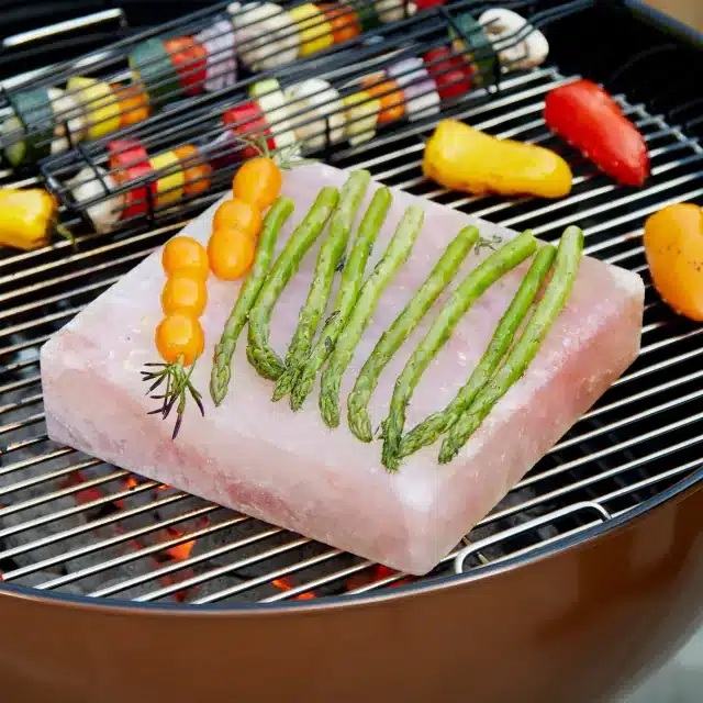 A slab of pink Himalayan salt on a grill with asparagus on top.
