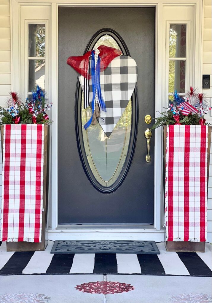 Close up view of red and cream table runners tucked into planters to decorate the front porch for July 4th.