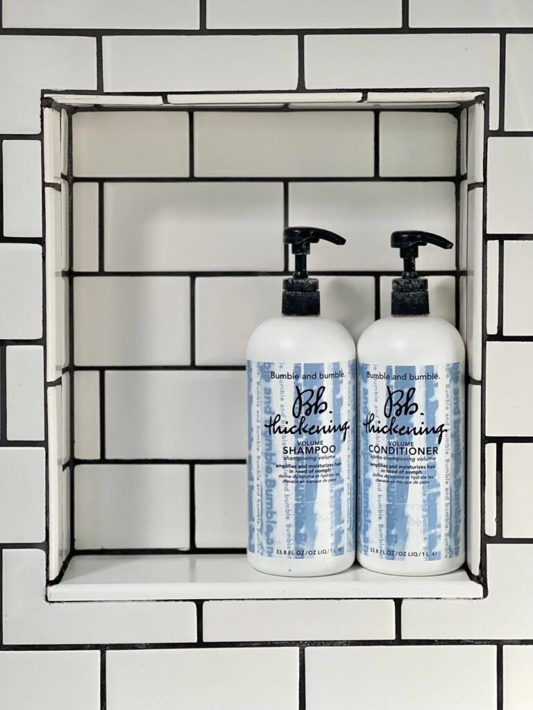 A bottle of shampoo and a bottle of conditioner placed in a shower niche.