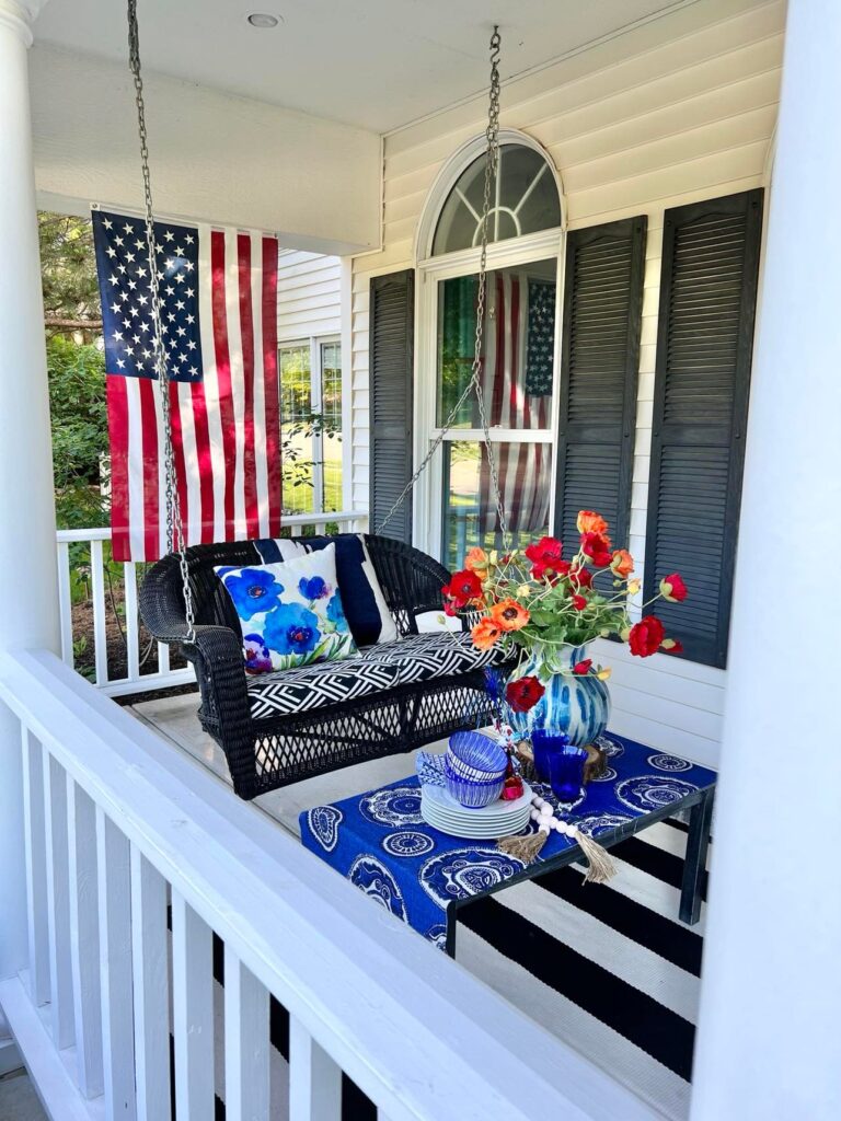 A side view of a black porch swing with floral pillow and faux poppy flower arrangement. 