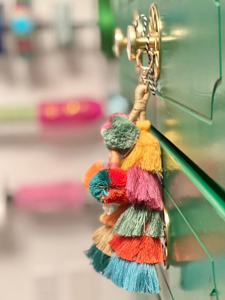 A close-up of a multi-colored pom-pom tassel hanging on the knob of the green dresser.