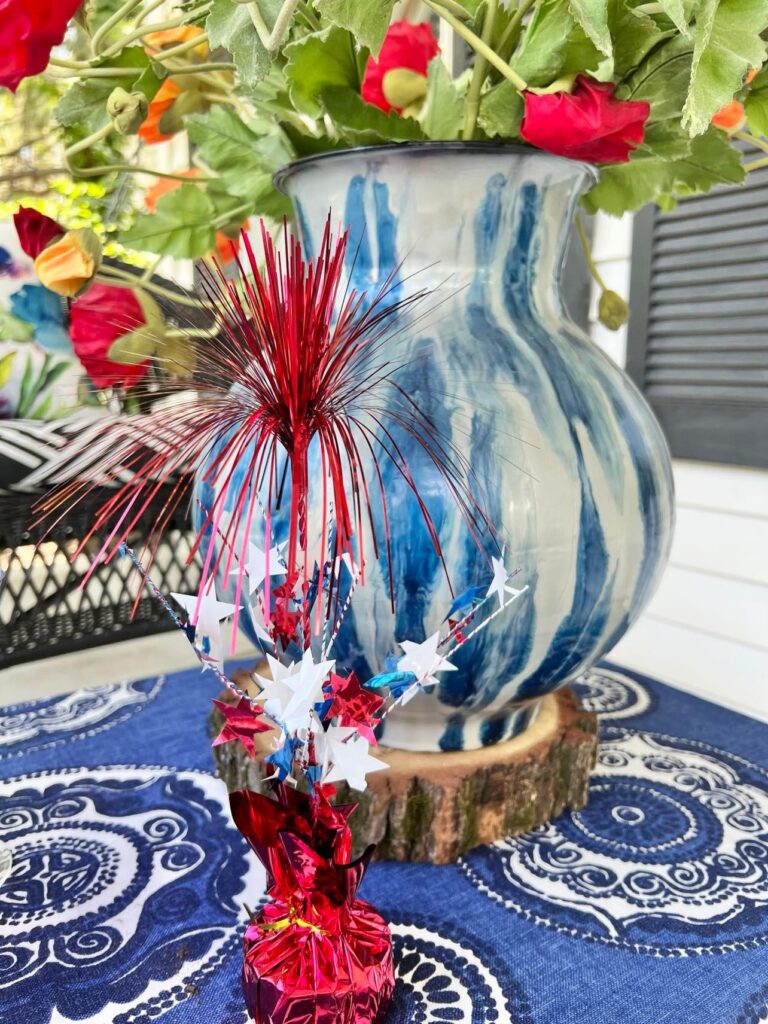 A blue and white abstract vase holding faux red and orange poppies as a focal point to decorate the porch for July 4th.