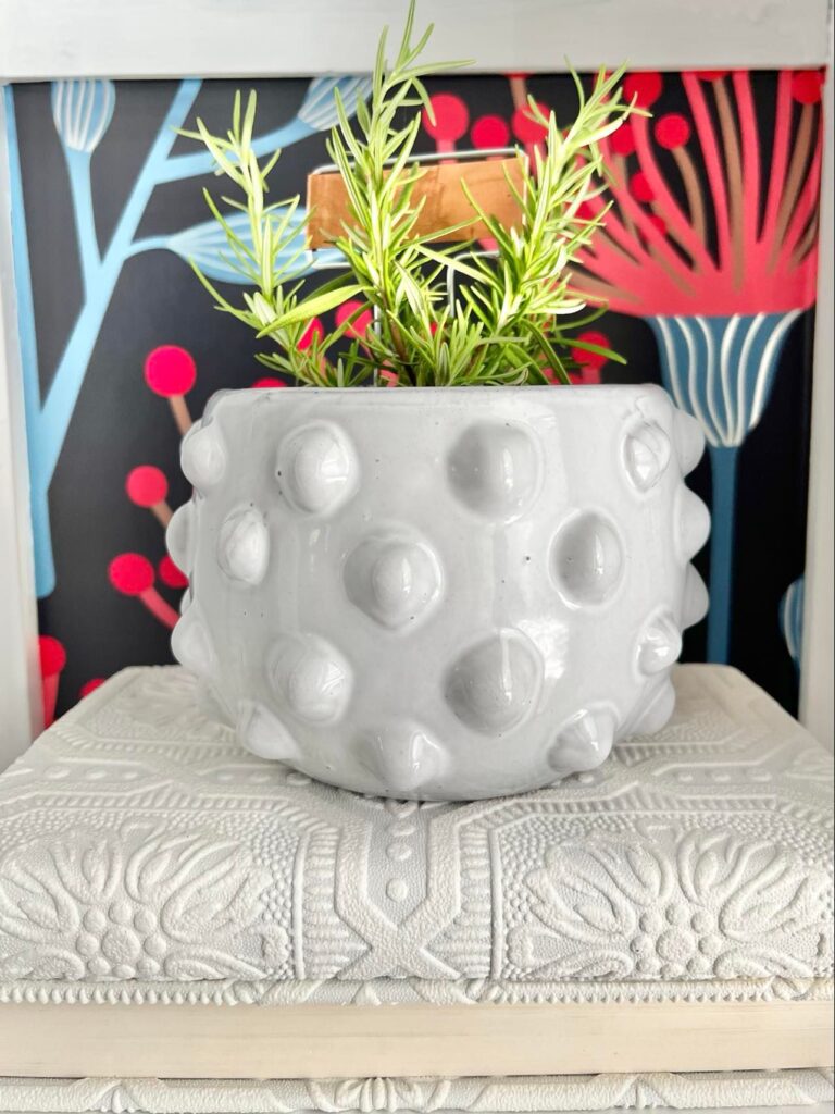A white pot sitting on top of a book really works when styling bookshelves for summer.