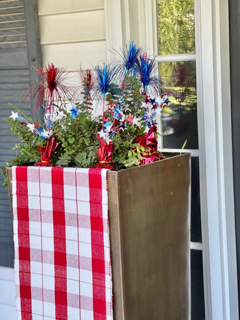 A green fern in a copper pot covered with a red and cream table runner.