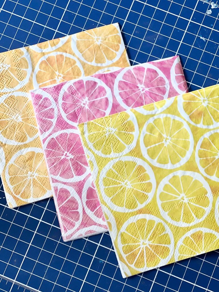 Three cocktail napkins with three colors of citrus fruits on the printed pattern.