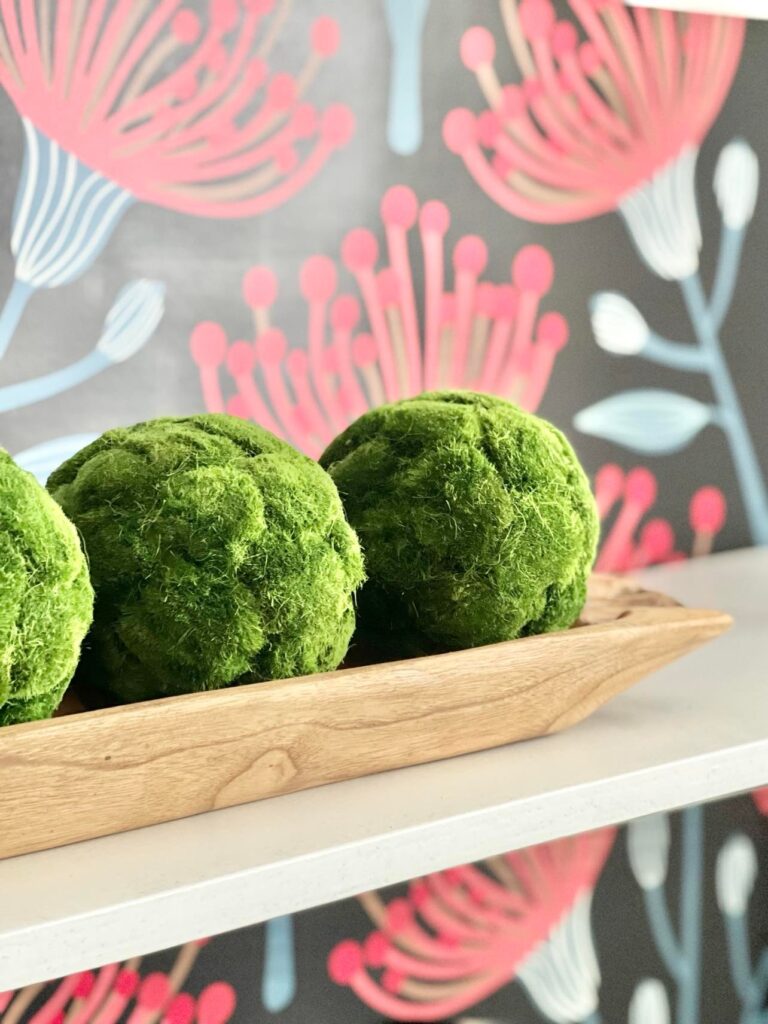 A wood dough bowl holding green faux moss balls.