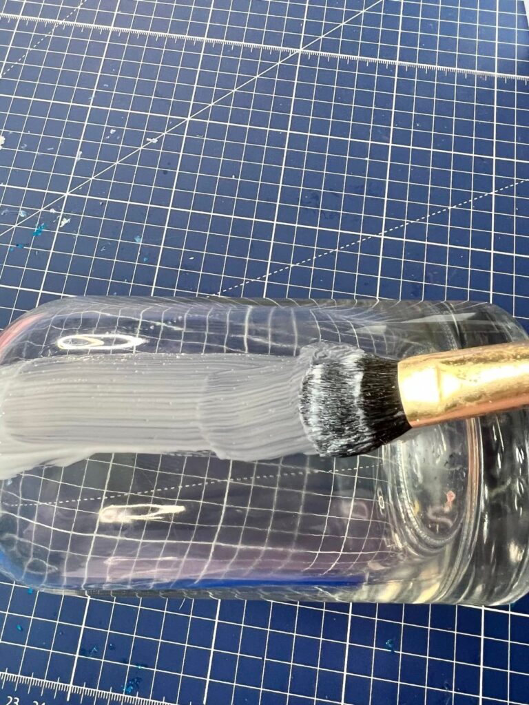 A brush applying a coat of decoupage glue onto the bottle.
Decoupage bottle idea.