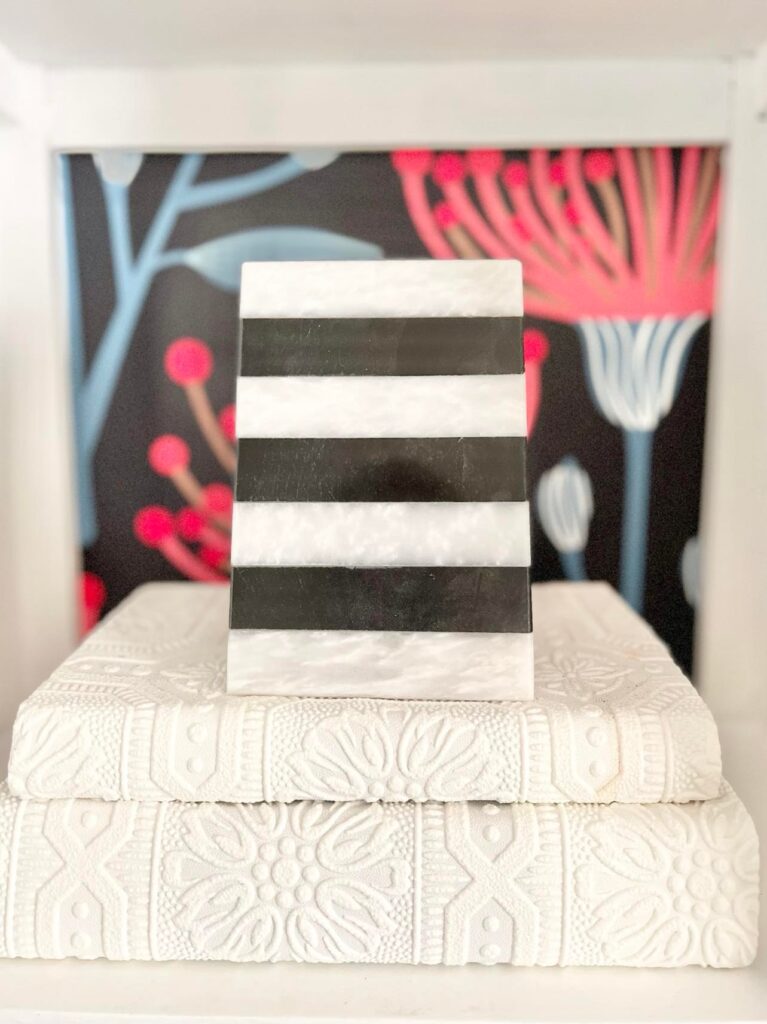 A black and white stipe bookend sitting on a stack of books works well when styling bookshelves for summer.