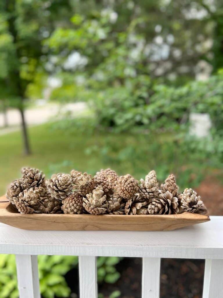 Bleached pinecones in a dough bowl on a white porch railing.