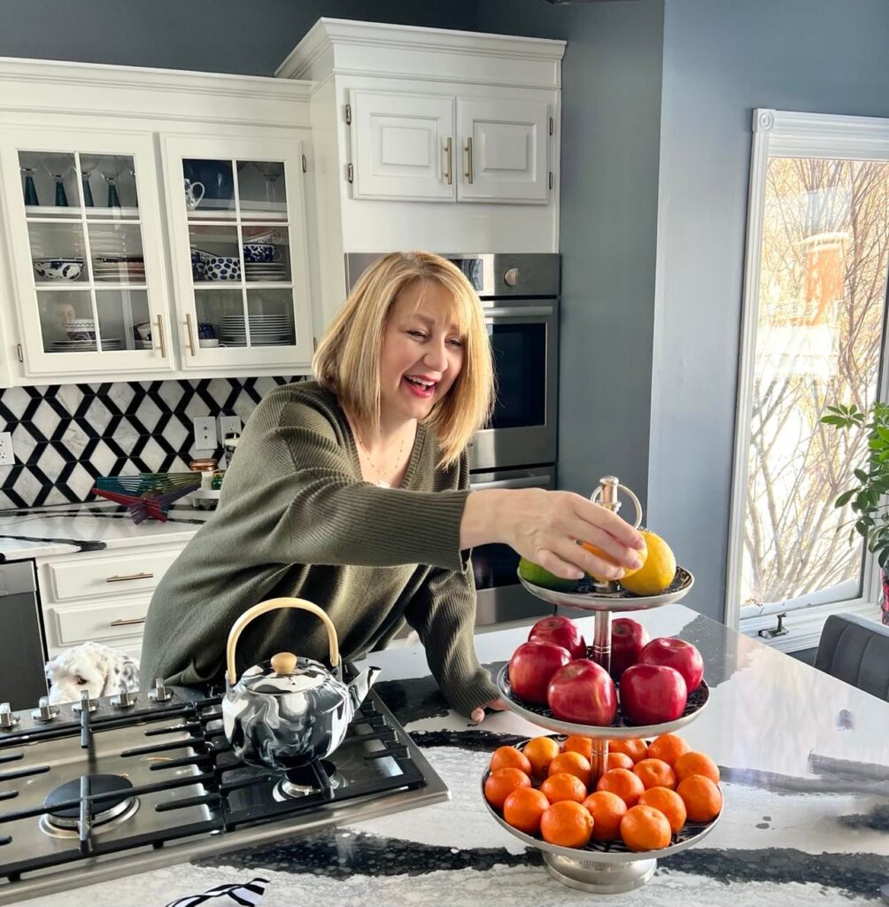 Missy displaying apples, oranges, and bananas as decor on a blue and white three tiered tray.