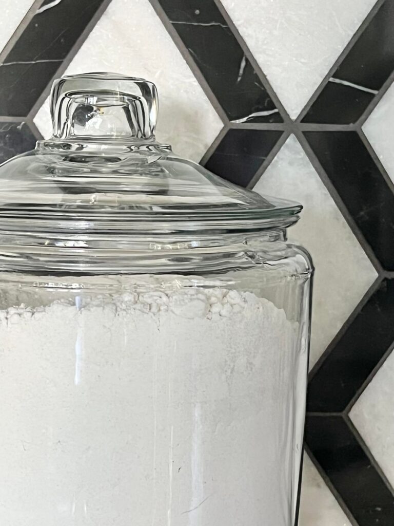 A glass kitchen canister sitting in front of black and white patterned backsplash tile.