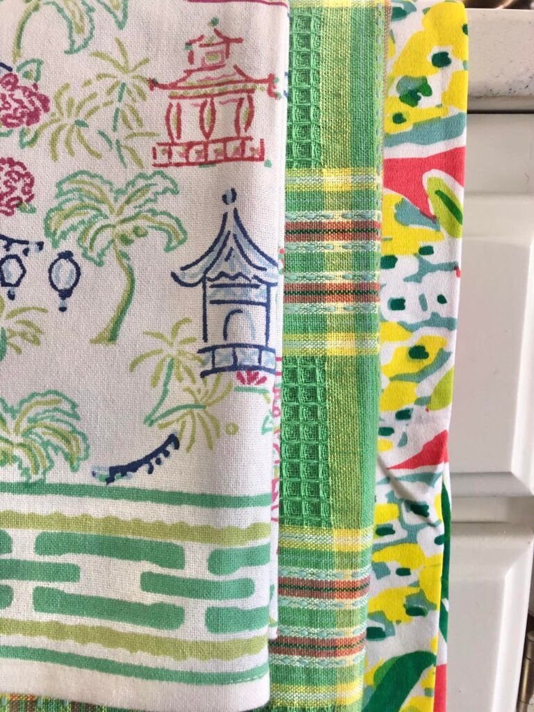 Three multi-colored tea towels draped as an accent on a kitchen sink.