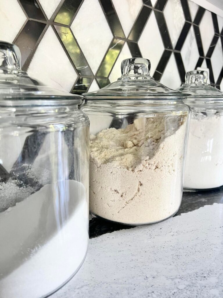 Clear glass canisters holding various flours and lined up on a kitchen counter.