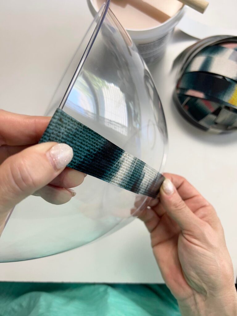 Applying the first strip of wallpaper to the plastic bowl.