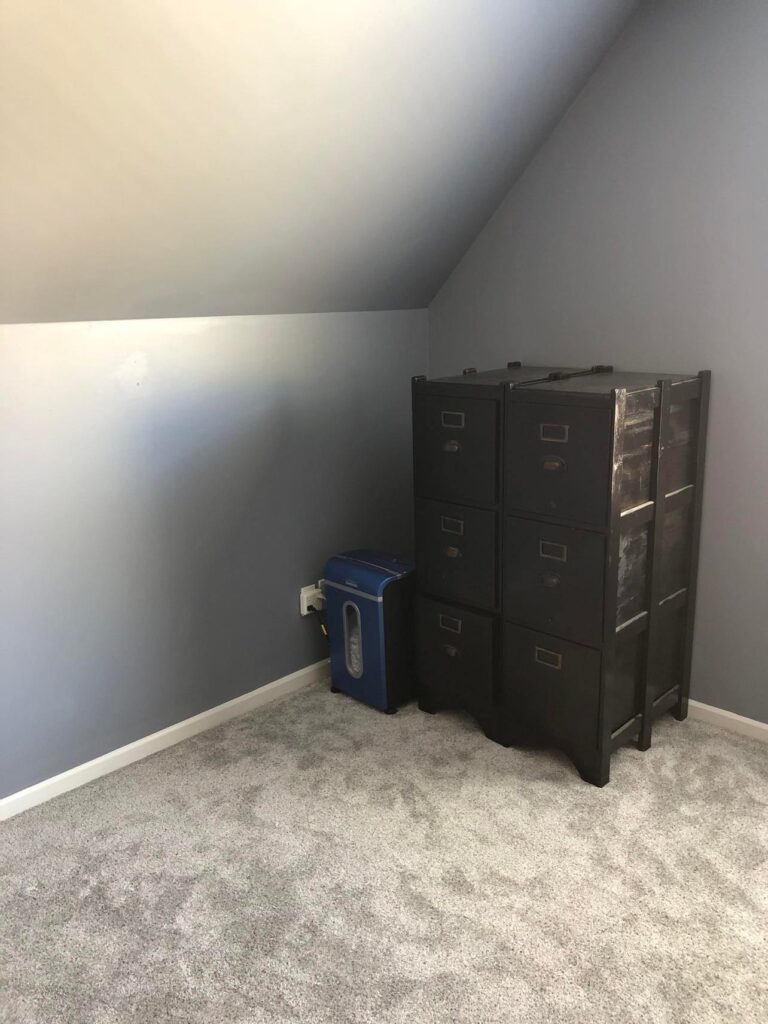 An empty, grey room with only a file cabinet an paper shredder.