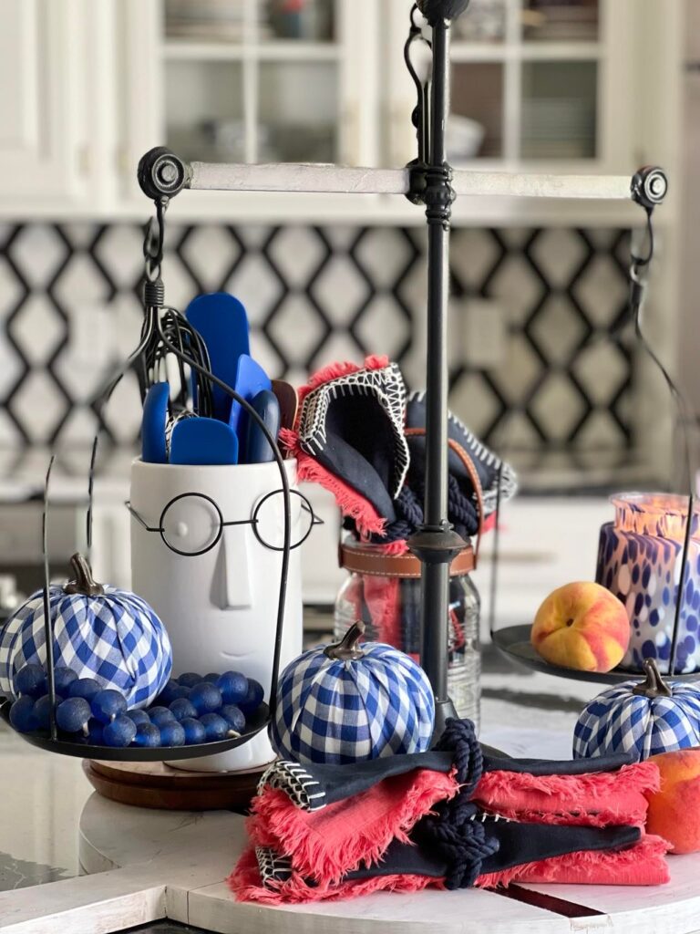 Kitchen balance scales holding blue and white gingham pumpkins surrounded by navy and coral cloth napkins.