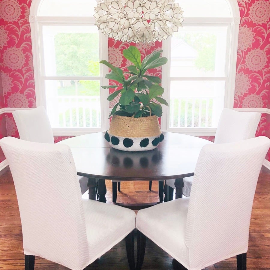 A fiddle leaf fig plant in a woven basket sitting on a dining room table.