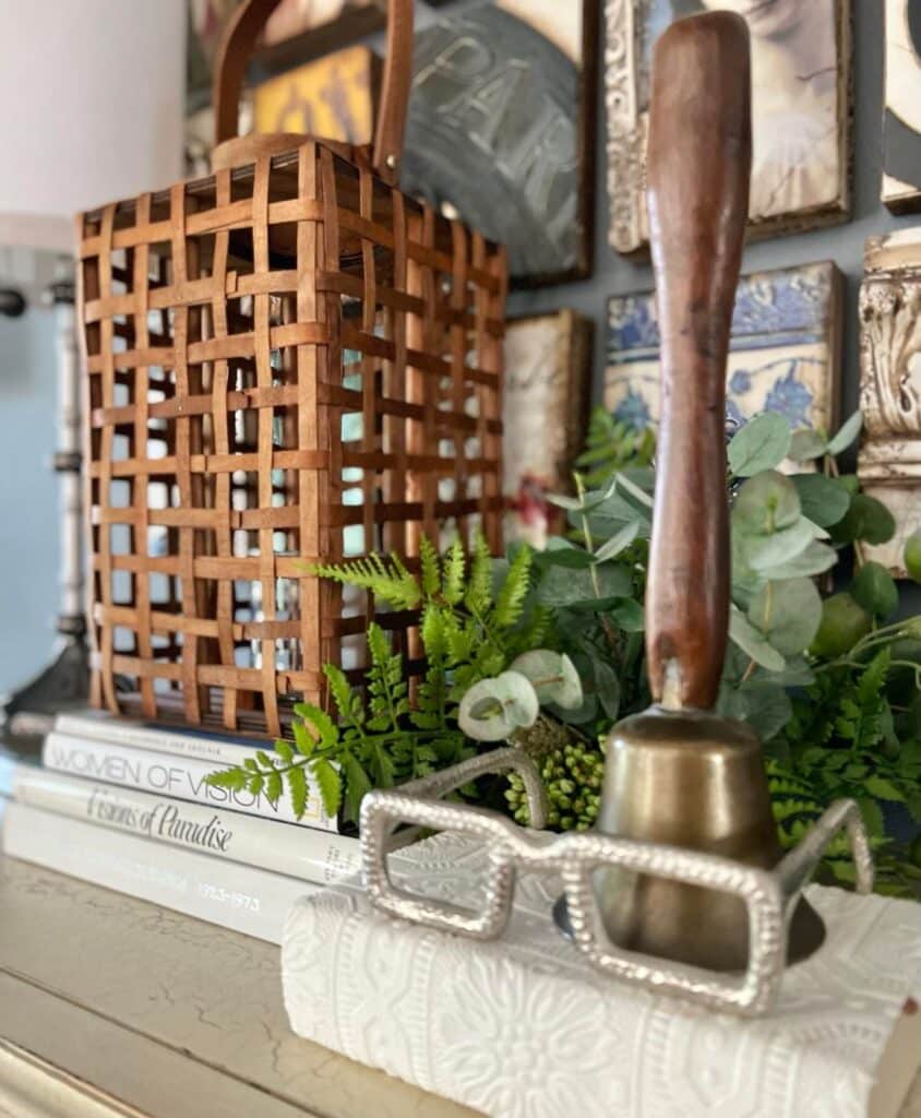 Fall home decor in wood tones sitting on a front entry chest with a schoolteacher bell.