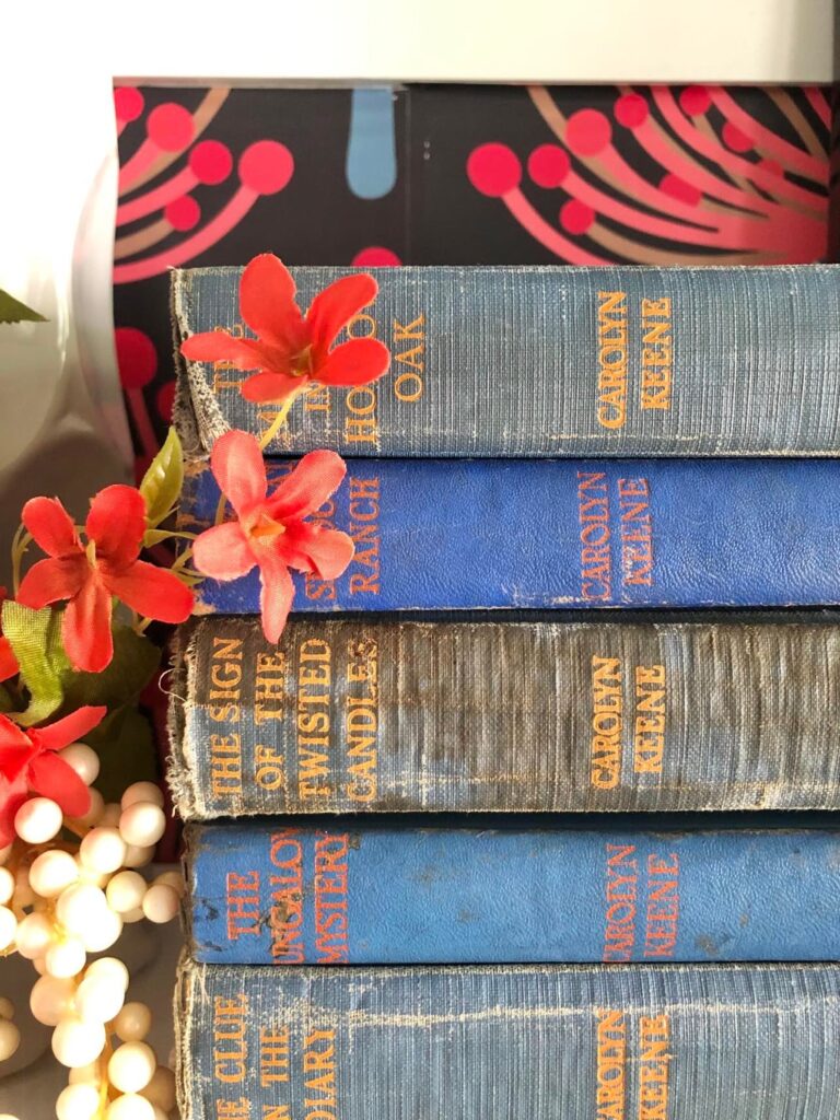 
A stack of vintage Nancy Drew books with navy blue and orange book covers.