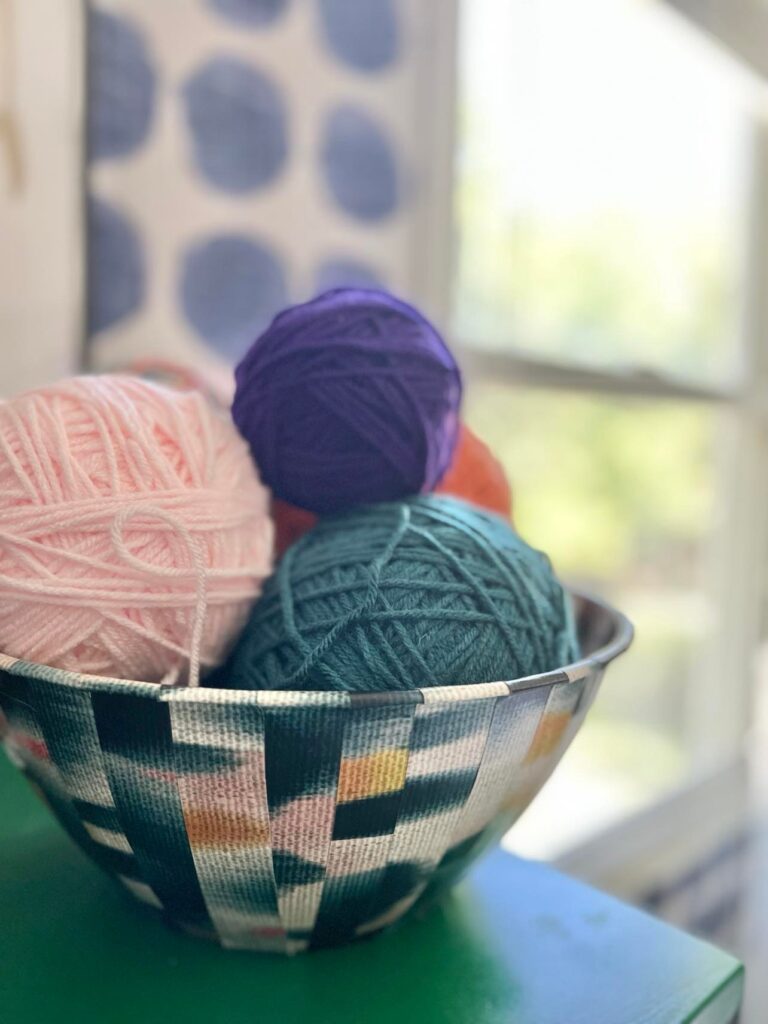 Multi-colored yarn balls piled into the decorative  bowl.