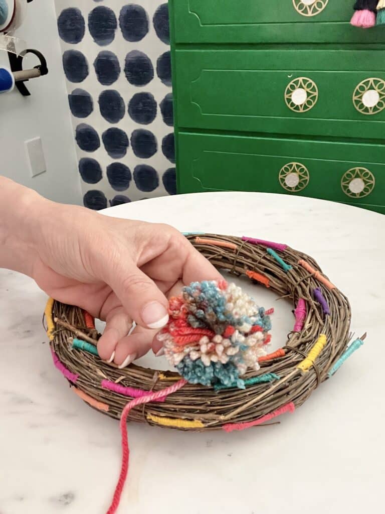 Adding a multi-colored pom pom to the wreath.