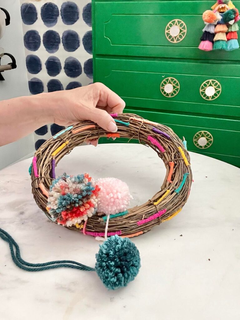 Adding two solid colored pom poms to the grapevine wreath.