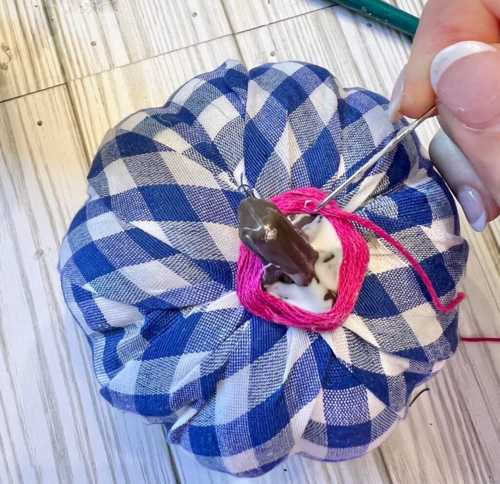 Winding and gluing pink embroidery thread to the stem of a faux pumpkin.
