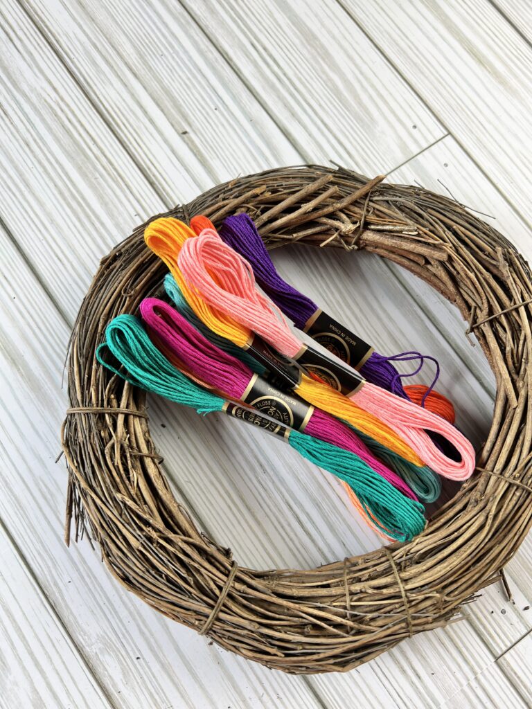 A grapevine wreath with several skeins of multi-colored embroidery thread.