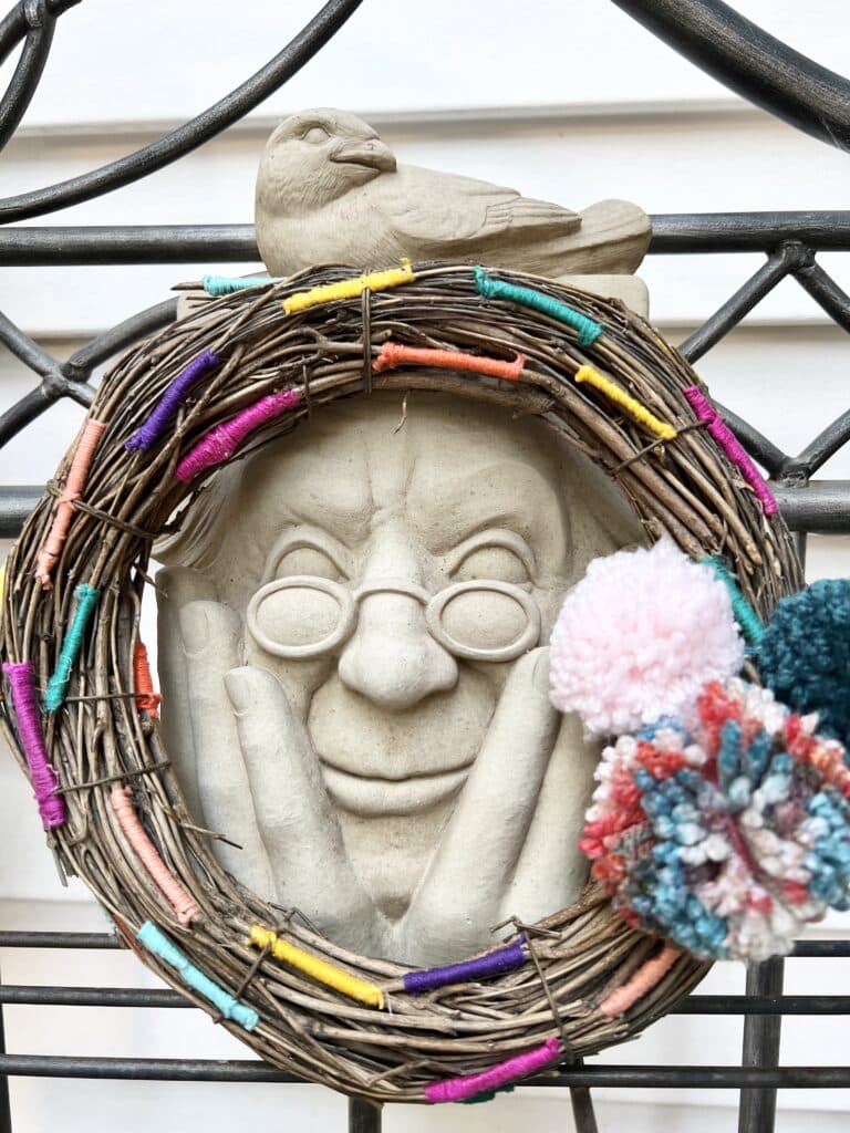 A grapevine wreath decorated with multi colored thread.