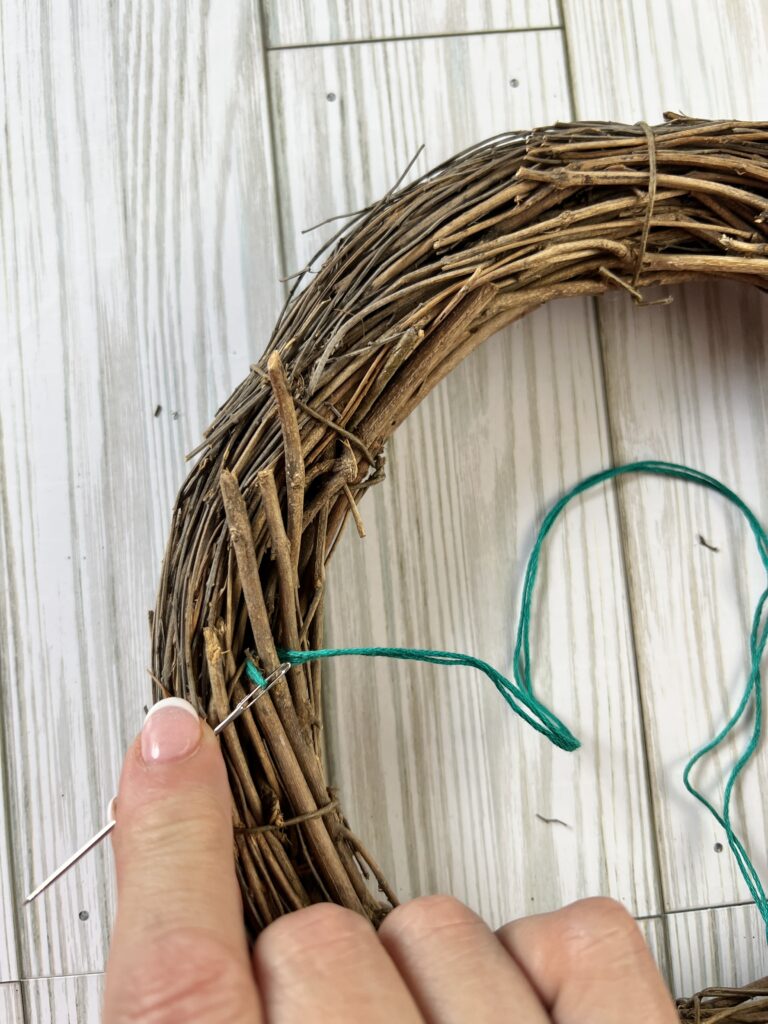 Using a needle to wrap the embroidery thread around an individual vine in the wreath.