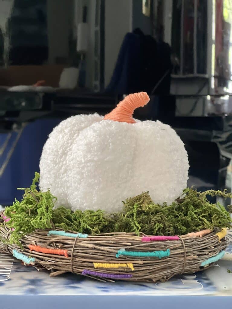 A decorative pumpkin sitting on top of the threaded grapevine wreath "nest".