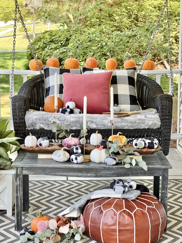 A porch swing decorated for Fall with pillows, throws and pumpkins in a dough bowl.