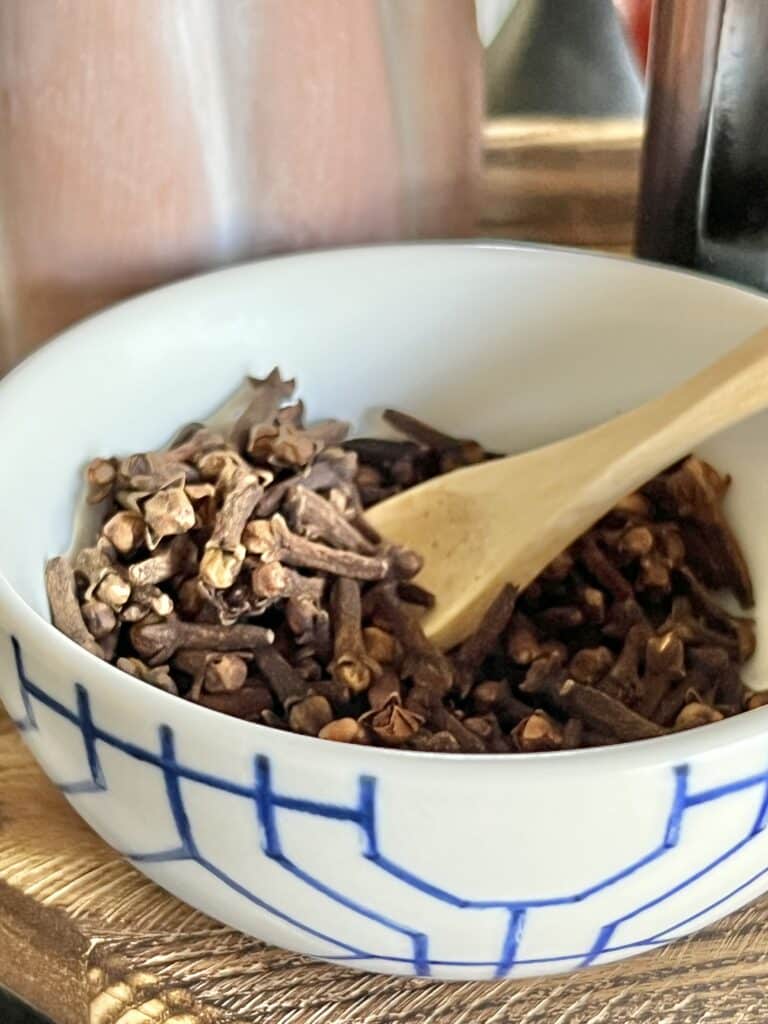 A bowl of whole cloves with a small wooden spoon.