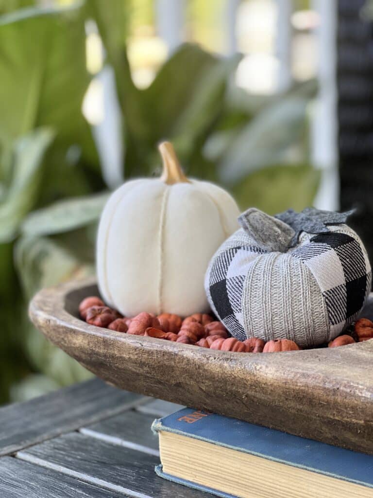 Two pumpkins sitting in a dough bowl on top of a vintage book.