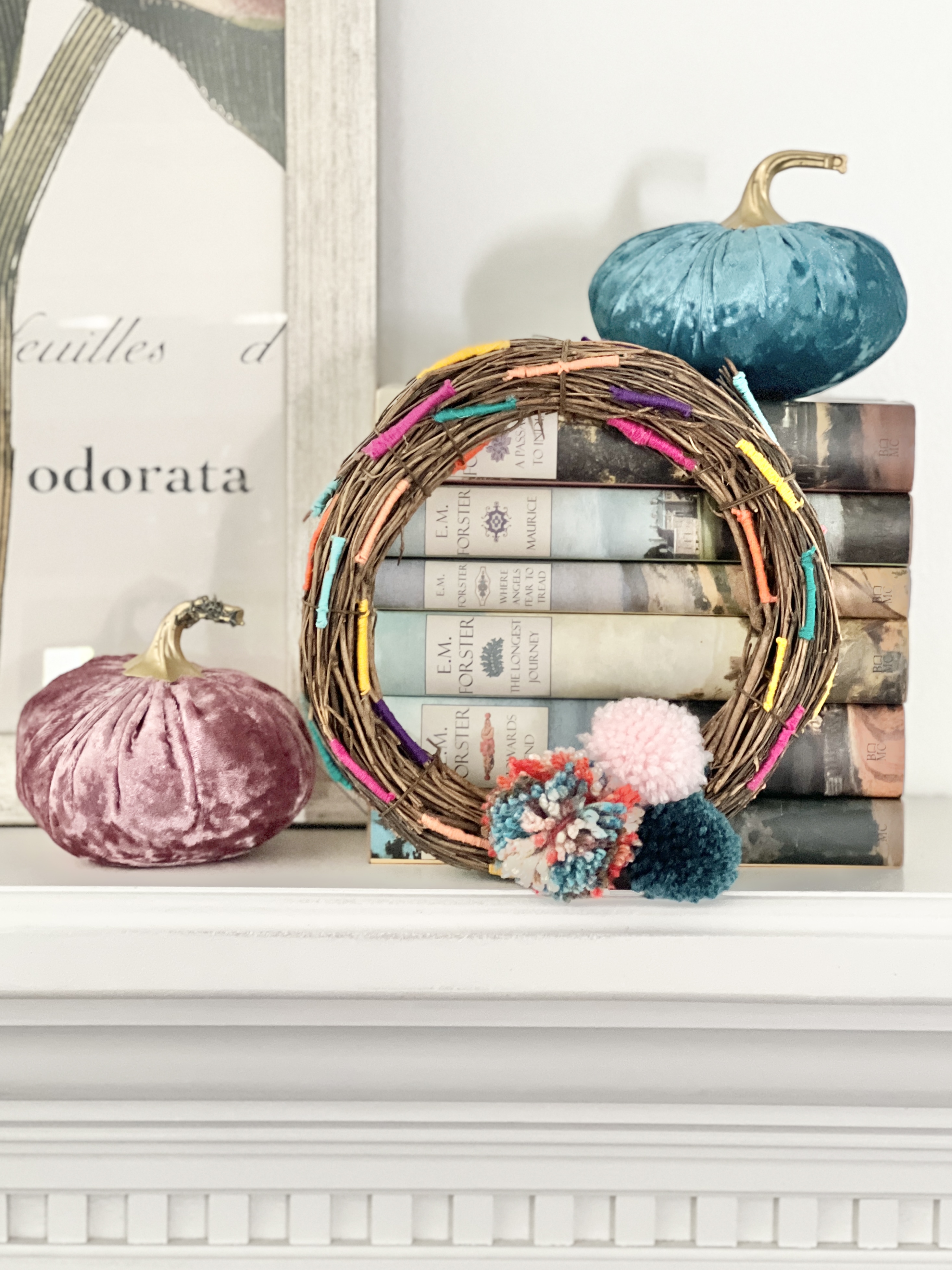 The threaded grapevine wreath sitting on a mantel surrounded by velvet pumpkins.