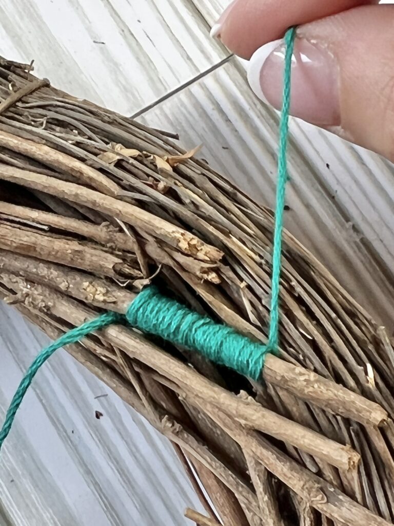 Turquoise embroidery thread wrapped around a vine in the wreath.