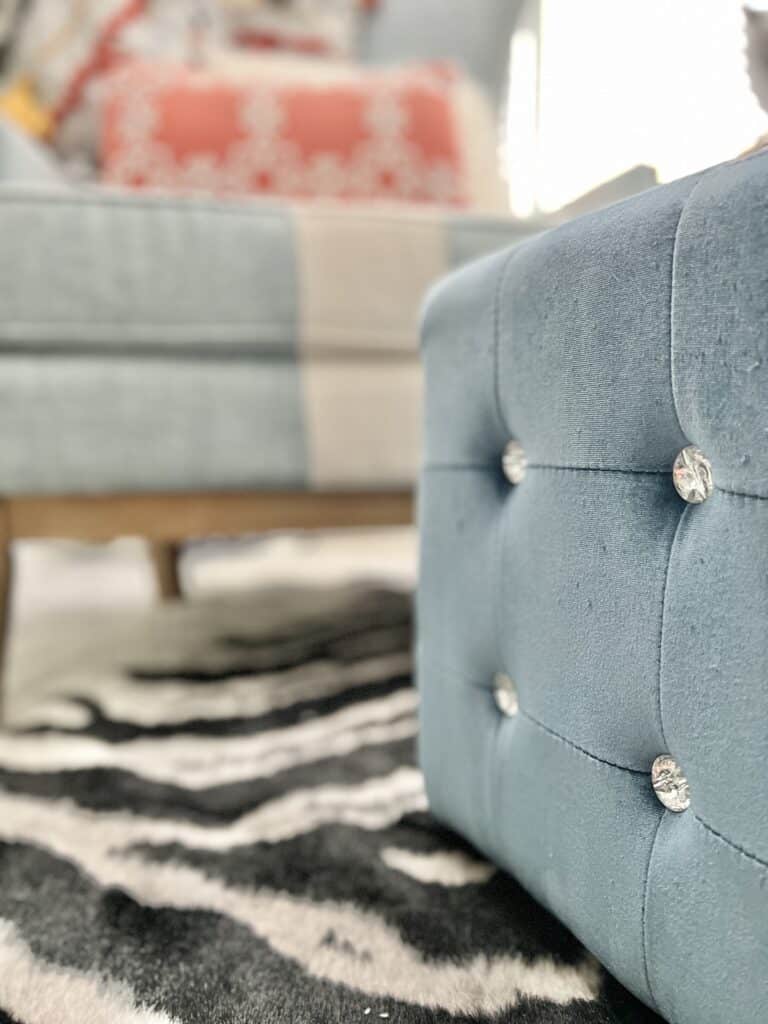 A blue ottoman sitting on a zebra pattern rug in the reading nook.