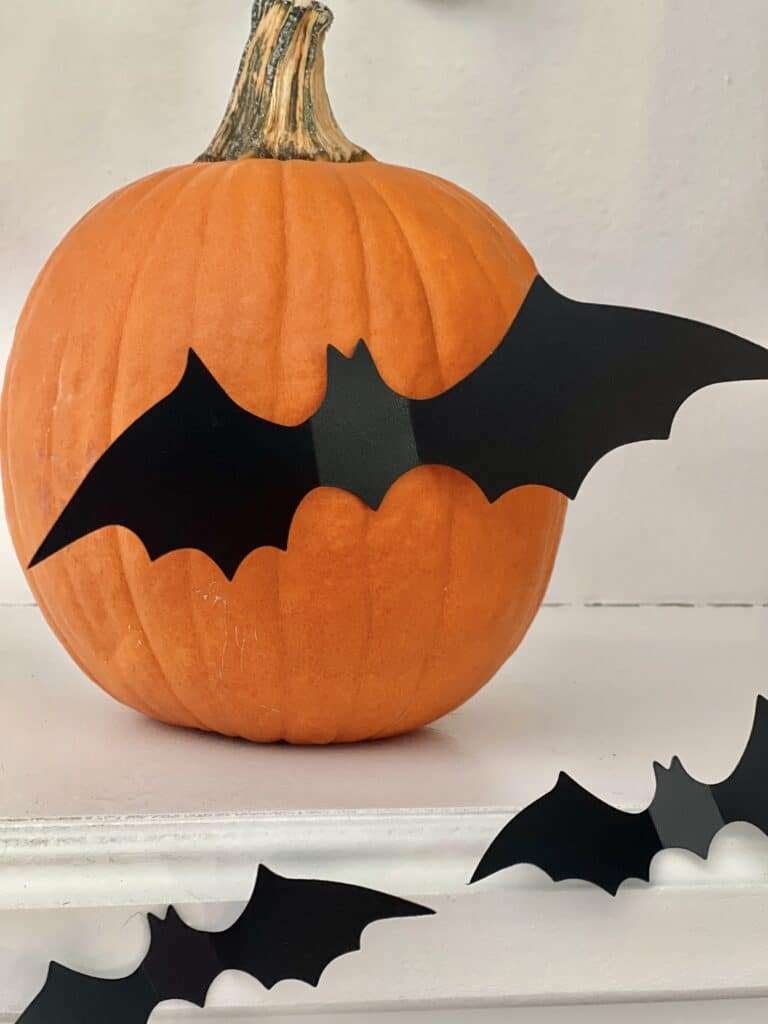 A plastic bat stuck to a pumpkin.