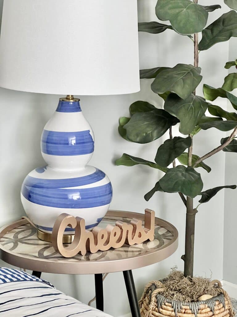A wooden cut-out of the word "Cheers!" sits on a bedside nightstand table in this colorful and cozy guest bedroom.