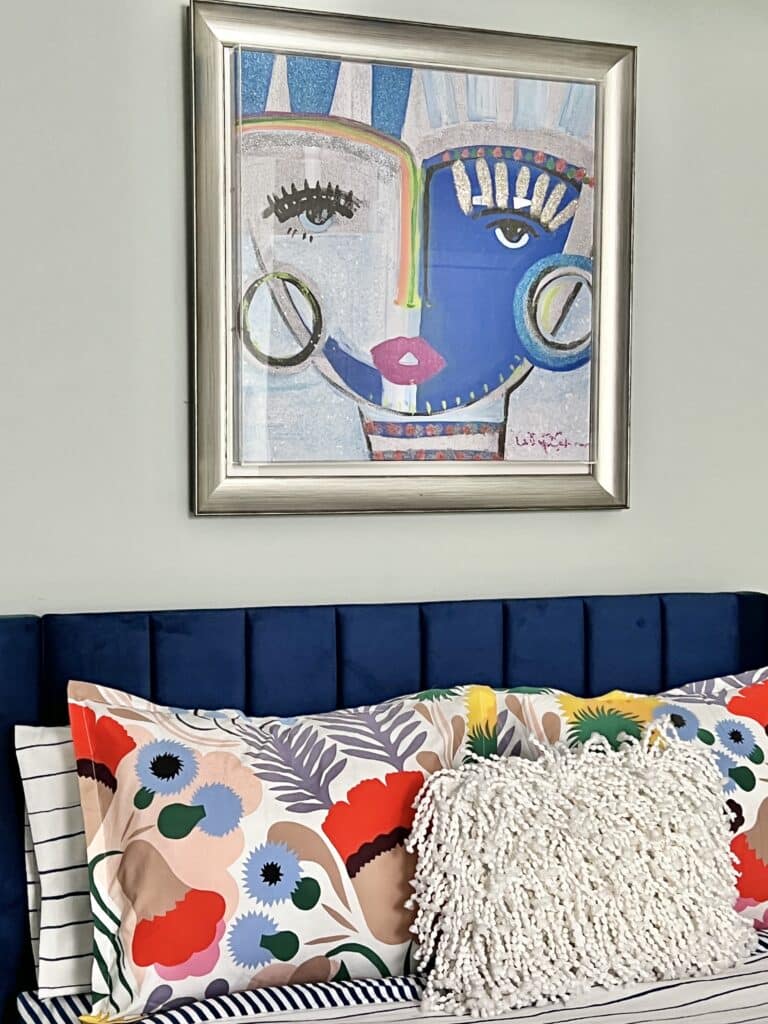 A bold and colorful wall art canvas by artist Windy O'Connor is hanging above a blue velvet headboard.