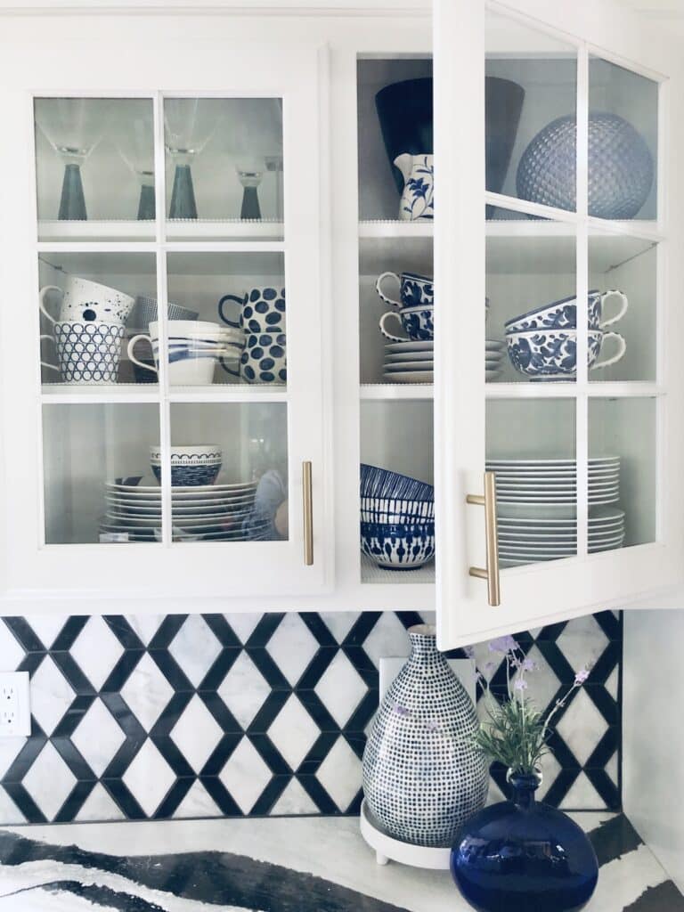 blue and white dishes styled in a glass kitchen cabinet with one door open.