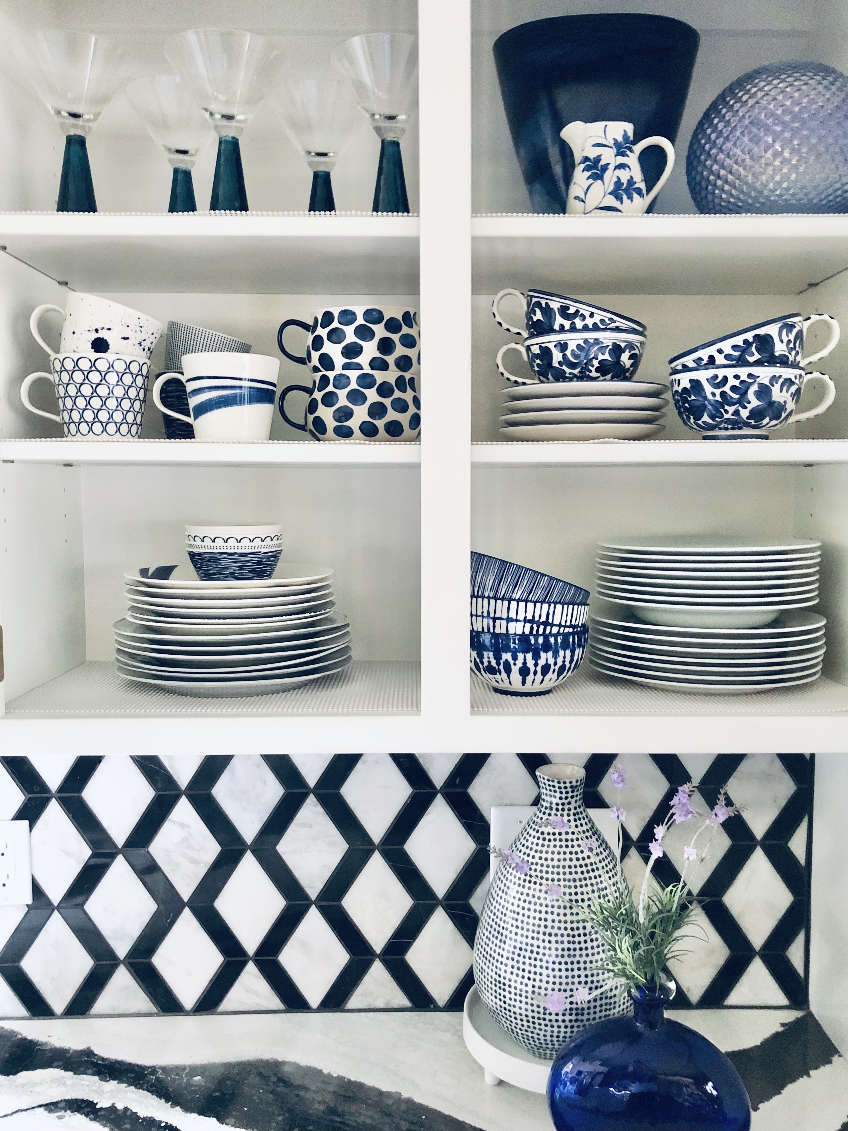 An array of blue and white white that have been styled to be seen through glass kitchen cabinets.